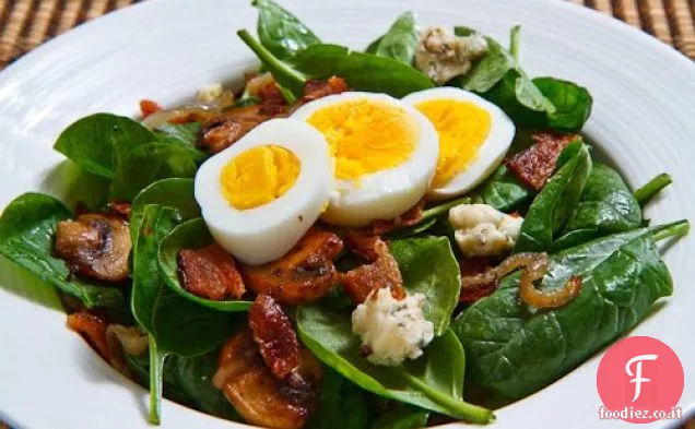 Insalata di spinaci con pancetta, cipolle caramellate, funghi e formaggio blu in una salsa di pancetta condita con un uovo sodo