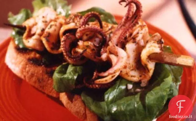Spiedini di calamari carbonizzati su pane tostato all'aglio con rucola
